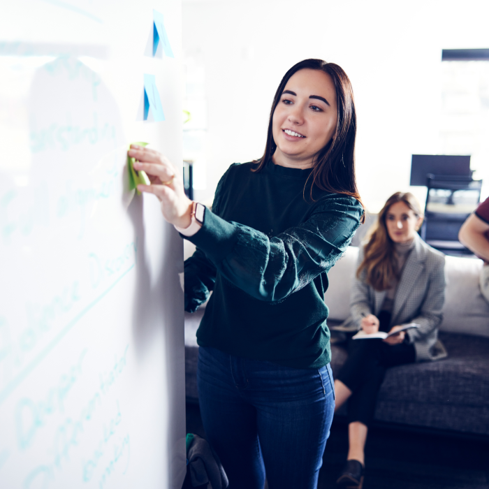 woman placing a post-it note on a whiteboard