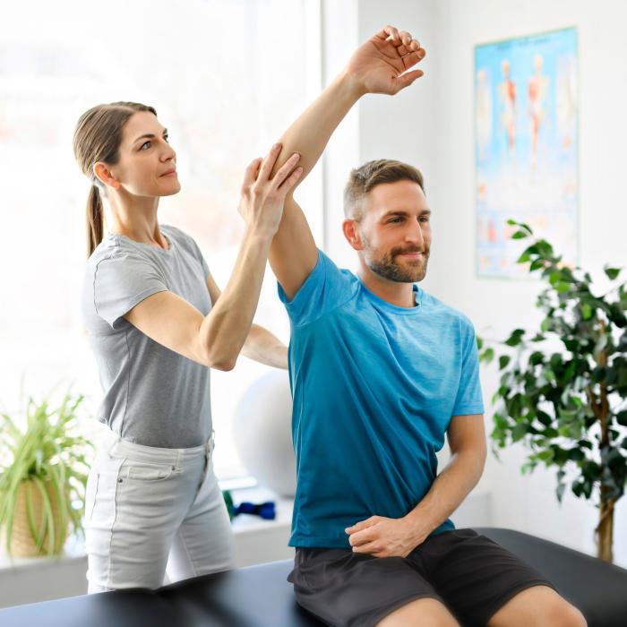 A physical therapist assisting a male patient with an arm stretch in a clinic