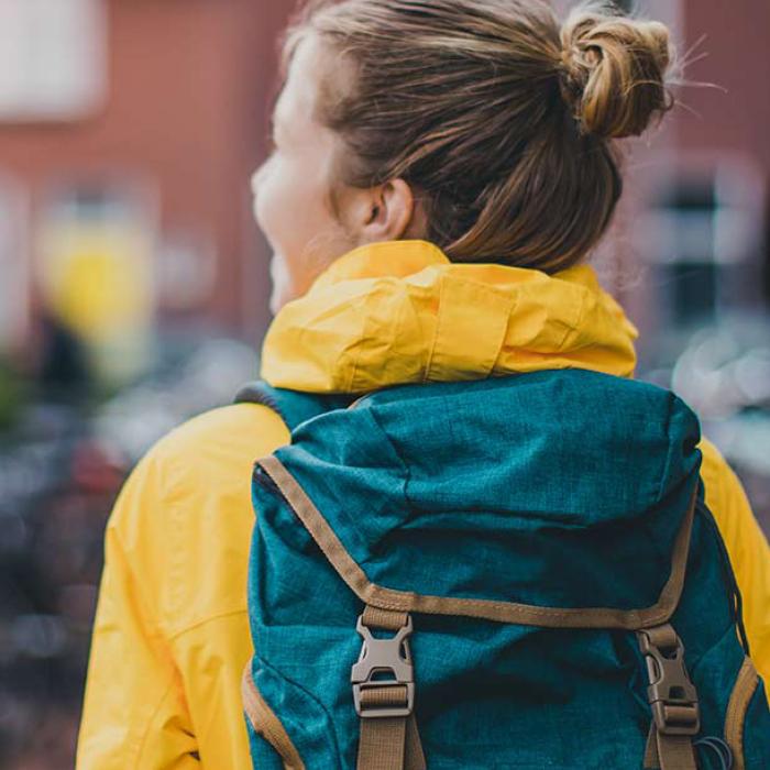 college student on campus in a yellow coat with green backpack not facing the camera