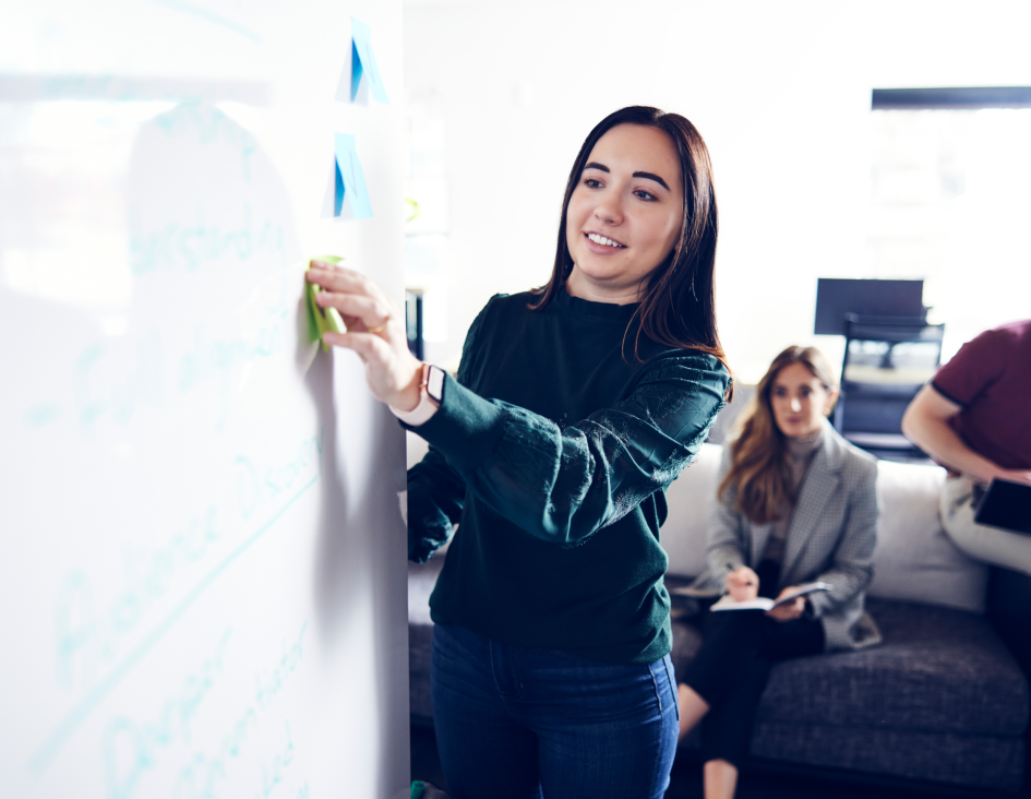 woman placing a post-it note on a whiteboard