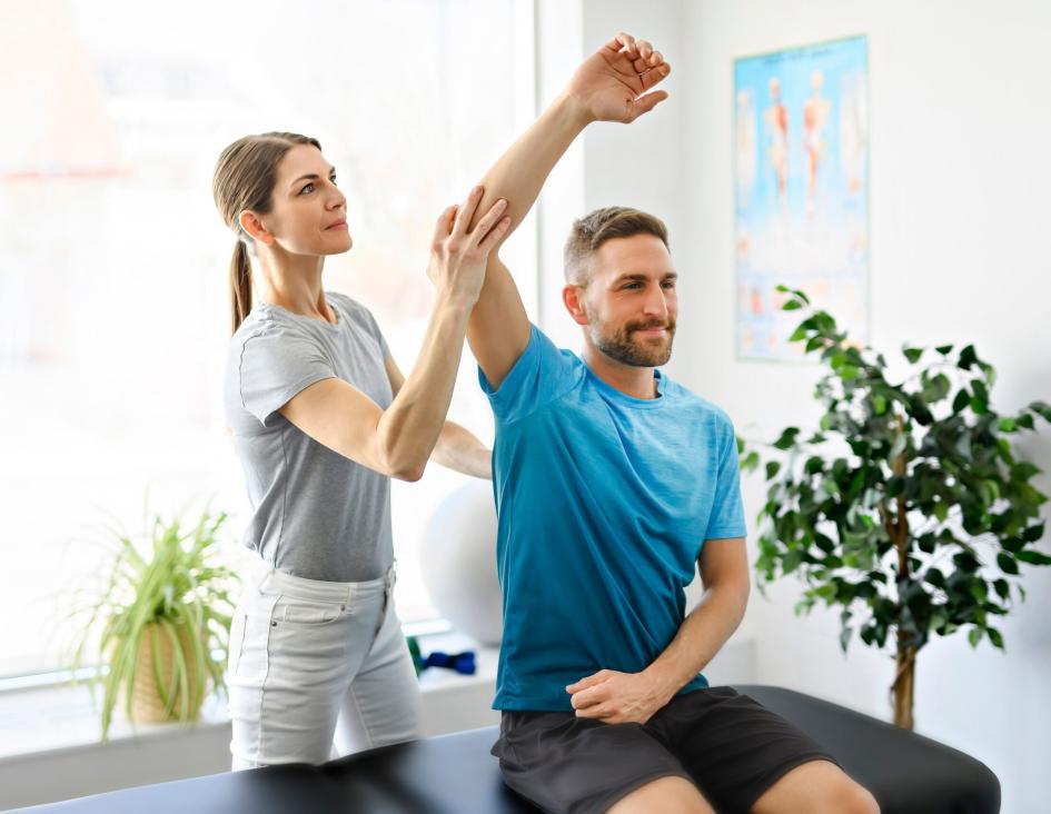 A physical therapist assisting a male patient with an arm stretch in a clinic